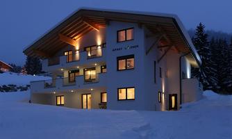 A modern apartment building in a snowy landscape at night. The windows are warmly lit, creating an inviting atmosphere.