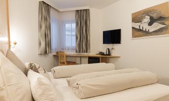 A cozy hotel room with two beds and modern furnishings. The room includes a desk, a television, and large windows with curtains.