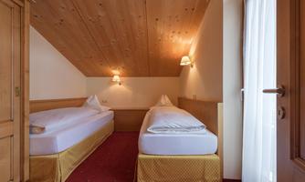 A cozy room with two single beds and wooden ceilings. The room has a warm atmosphere and plenty of daylight.
