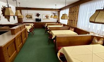A cozy restaurant with tables and chairs covered with yellow tablecloths. The walls are decorated with pictures and large windows let in a lot of light.