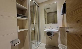 A modern bathroom with a shower cabin, a sink, and a large mirror. The walls are bright and the decor is simple and functional.