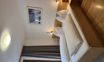A modern bedroom with two single beds, illuminated by stylish bedside lamps. Large windows provide a view of nature and create a bright, inviting atmosphere.