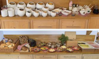 A rich breakfast buffet with various muesli and yogurt bowls on top. Below are fresh rolls, cold cuts, cheese, and fruit arrangements.
