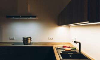A modern kitchen with a wooden countertop and minimalist furnishings. There is a stove, a sink, and some ingredients on the table.