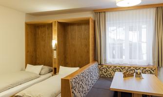 A modern room with two single beds and a cozy dining area. Large windows let in plenty of light and create an inviting atmosphere.