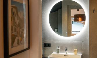 A modernly designed bathroom with a round mirror and elegant sink. The walls are simple, and the lighting creates a pleasant atmosphere.