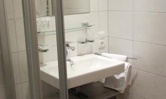 A modern bathroom with a shower and a sink. The walls are light tiled and there is a small rug on the floor.
