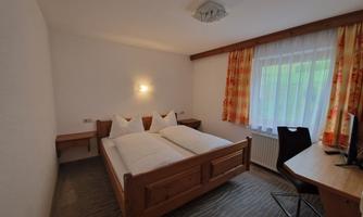 A cozy bedroom with a double bed and a desk. Large windows provide ample daylight.