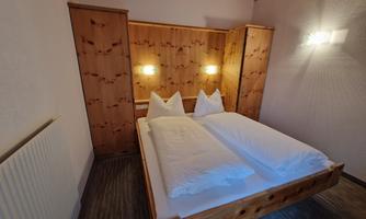 A cozy bedroom with a wooden bed and two pillows. The walls are light, and there is soft lighting on the sides.