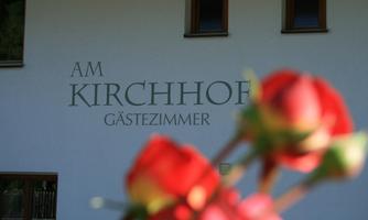 A building with the inscription "Am Kirchhof Guest Rooms". In the foreground, there are blurry red roses.