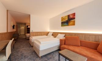 A modern hotel room with two single beds and a cozy orange sofa. The walls are painted light and adorned with a piece of artwork.