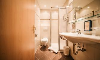 A modern bathroom with a shower, sink, and toilet. The walls are bright and the furnishings are functional.