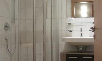 A modern bathroom with a shower cabin and a sink. The walls are tiled and the floor is brown.