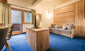 A cozy room with wooden furniture and blue carpeting. Large windows provide plenty of daylight and a pleasant atmosphere.
