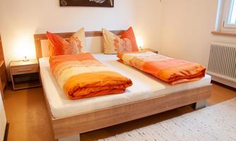 A cozy bedroom with a double bed and orange pillows. Soft light from the bedside lamps creates an inviting atmosphere.