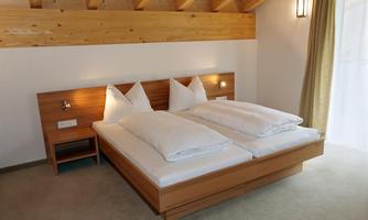 A cozy bedroom with a double bed and white bed linen. The wooden ceiling and soft lighting create a relaxed atmosphere.