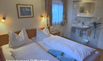 A cozy bedroom with two single beds and natural light. There is a bathroom with a sink and mirror.