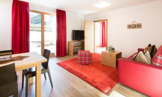 A cozy living room with a red carpet and sofa. Large windows let in plenty of light and offer a view outside.
