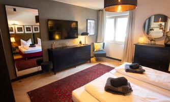 A modern room with two beds and a large mirror. There is a television, a cozy seating area, and artworks on the wall.