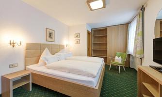 A bright bedroom with two single beds and a comfortable chair. The walls are painted in neutral tones, and there is ample storage space.