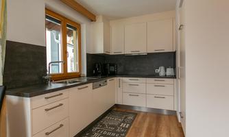 A modern kitchen with bright cabinets and a countertop made of gray material. Large windows let in plenty of daylight.