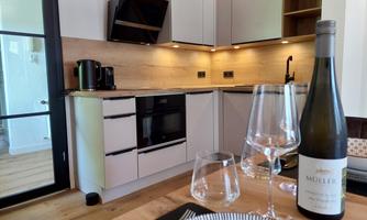 A modern kitchen with wood and refrigerator elements. On the table are wine glasses and a bottle of wine.