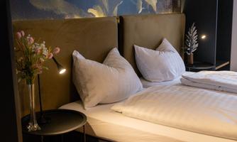 A modern bedroom with a large bed, soft pillows, and a stylish bedside lamp. A bouquet of flowers on the nightstand complements the cozy atmosphere.