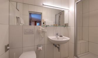 A modern bathroom with bright tiles and a shower. There is a sink with a mirror and towels.