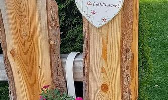 A beautiful wooden fence with a heart-shaped sign and a flower box full of pink flowers. The surroundings are green and inviting.