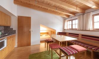A cozy kitchen with wooden elements and a dining area. The room has large windows and a warm, inviting charm.