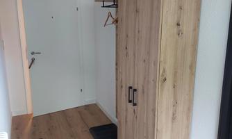 A bright hallway with a modern wooden wardrobe and space for coats. The floor is made of light wooden planks and there are two doormats.