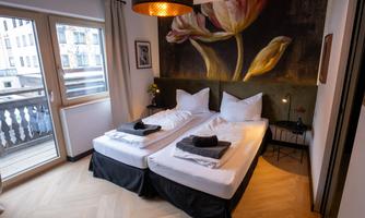 A modern bedroom with two single beds and minimalist decoration. A large artwork featuring floral motifs hangs on the wall.