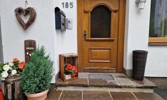An inviting front door with wood cladding and a numbered sign. Flowers and plants in pots decorate the entrance area.