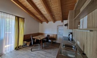A cozy room with a wooden beam ceiling, a table and chairs. The kitchen is equipped with modern appliances and there are large windows that let in plenty of light.