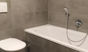 A modern bathroom with gray tiles, a bathtub, and a toilet. The furnishings are simple and functional.