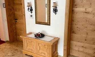 An inviting entrance area with wooden doors and a decorative mirror. On the dresser, there is a small floral arrangement, and the floor is covered with a beautiful rug.