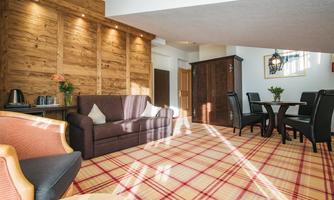 A cozy room with wooden paneling and a sofa. The area includes a table with chairs and is decorated with a checkered rug.