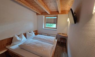 A cozy room with two beds and wooden furniture. The walls are bright and there is a window with a view outside.