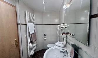 A modern bathroom with a sink, a large mirror, and towels. The walls are brightly tiled and the decor is minimalistic.