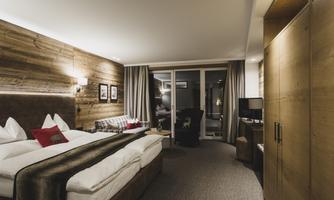 A modern hotel room with a large double bed and cozy furnishings. Large windows offer a view of the outdoors.