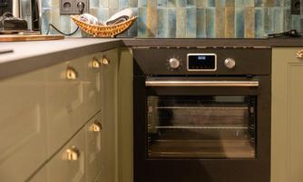 A modern kitchen with an elegant oven and beautiful tiles in the background. The furniture is in soft shades of green.