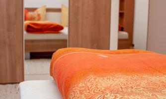 A cozy bedroom with an orange ceiling. In the background, wooden wardrobes and a bed are visible.