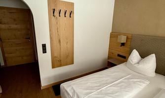 A modern hotel room with two beds and a wooden ceiling. In the background, there is a door and a wardrobe on the wall.