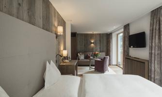A modern room with a comfortable bed and stylish furniture. The room offers a view of a cozy seating area and has large windows for plenty of daylight.