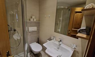 A modern bathroom with a shower, sink, and toilet. The walls are painted in neutral colors and there are wooden shelves for towels.