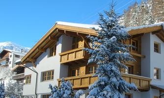 A modern chalet in winter, surrounded by snow and fir trees. The clear blue sky gives the scene a fresh atmosphere.
