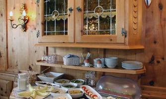 A rustic buffet with various dishes, including cheese, vegetables, and snacks. In the background, there is a wooden cabinet with glass doors and crockery.