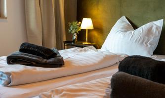 A cozy bedroom with a large bed and clean bedding. Folded towels are placed on the bed, and a lamp provides warm light.
