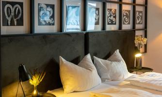 An elegant bedroom with a large bed and decorative pillows. Several pictures in modern frames hang on the wall.