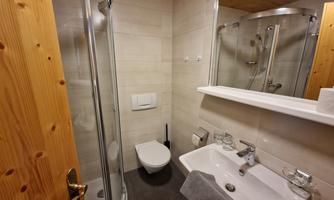 A modern bathroom with a shower, sink, and toilet. The walls are light, and there are wooden details that create a cozy atmosphere.